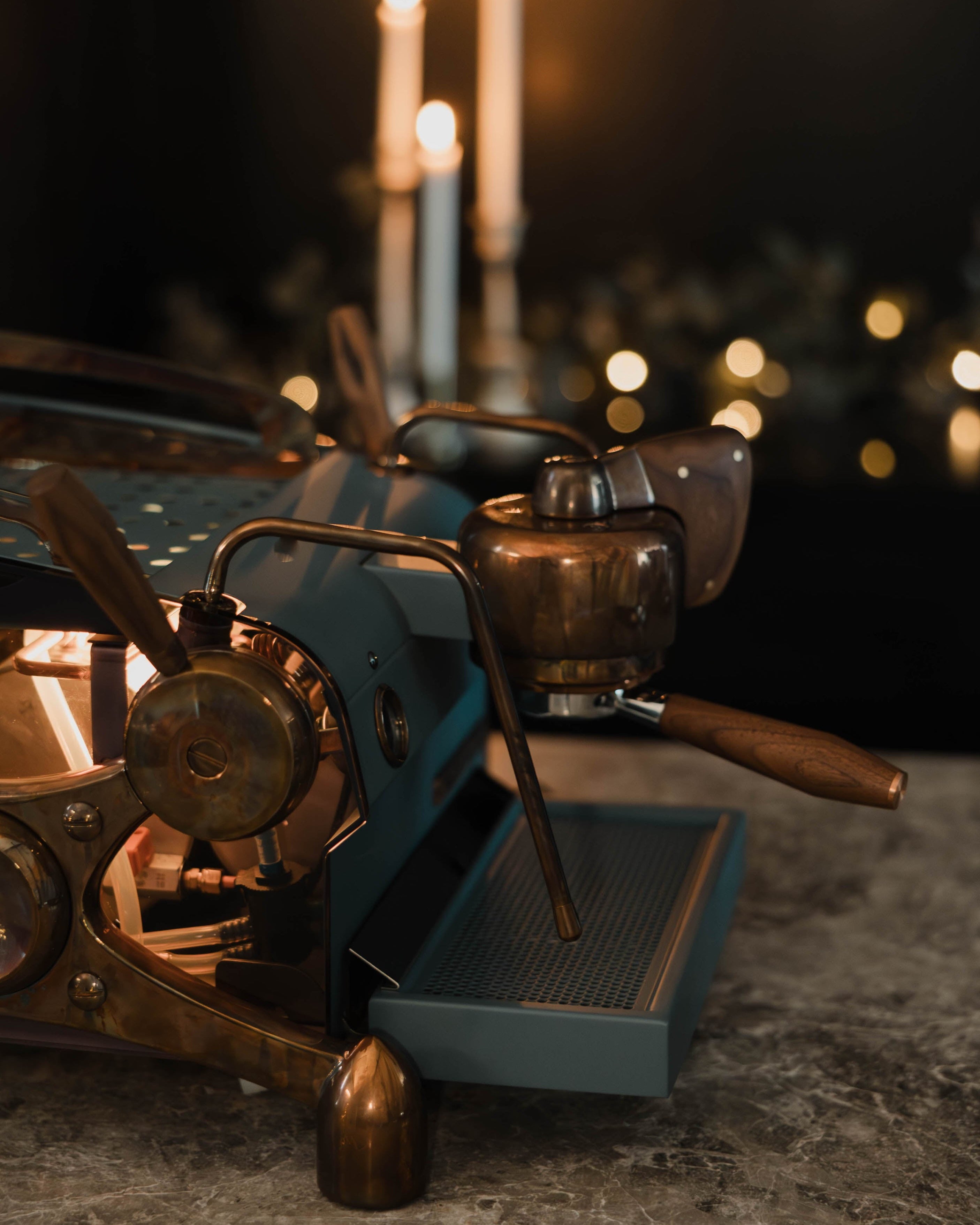 The side of a deep blue, bespoke Slayer Single Group espresso machine with burnt copper highlights and walnut accents, showing its lit interior through smoky side panels.