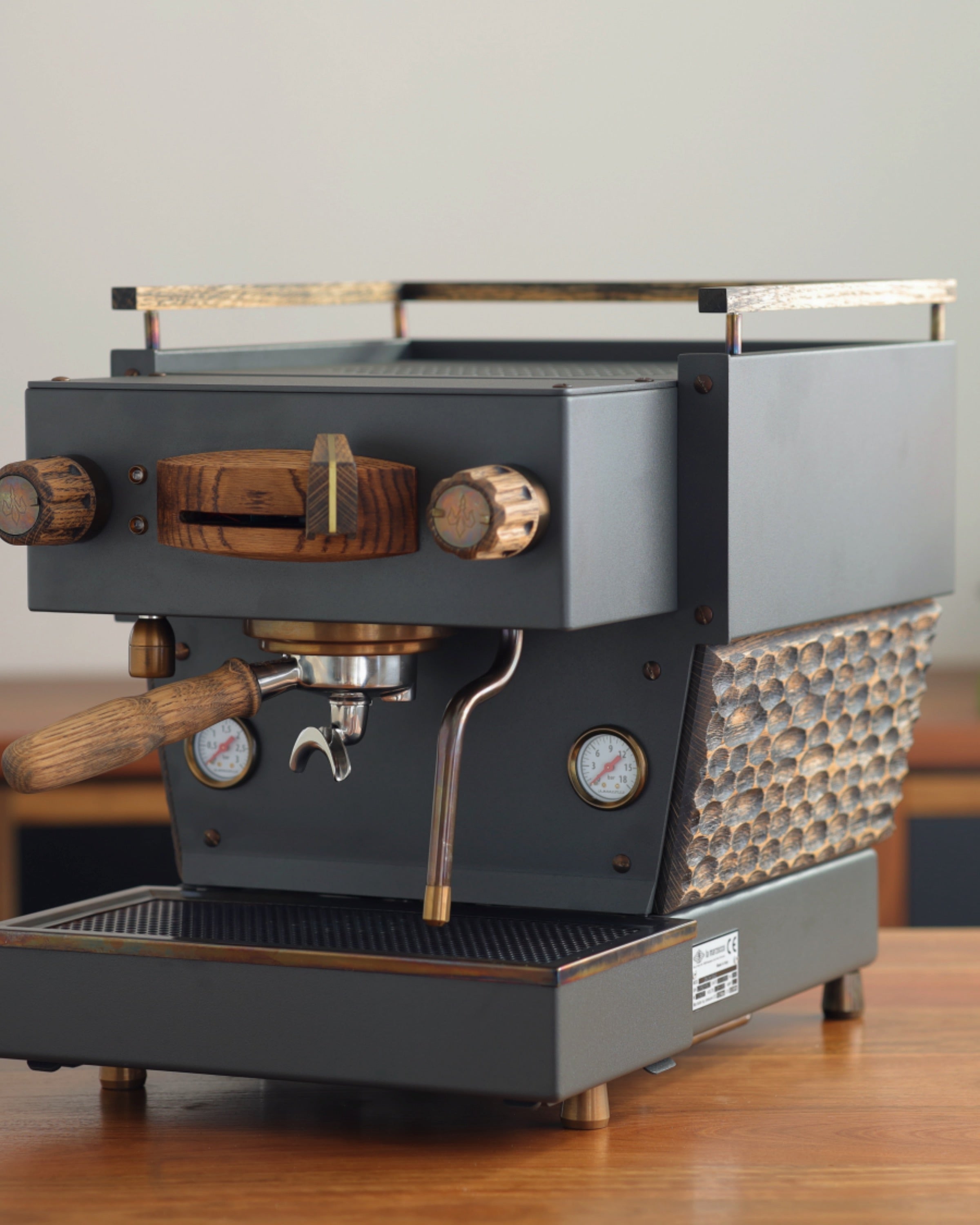 A weathered-slate grey Specht Linea Mini with a hand-carved, aged-oak mid-section, and bronze highlights.