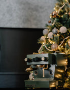 A dark green Linea Micra with brass highlights, underneath a Christmas tree.