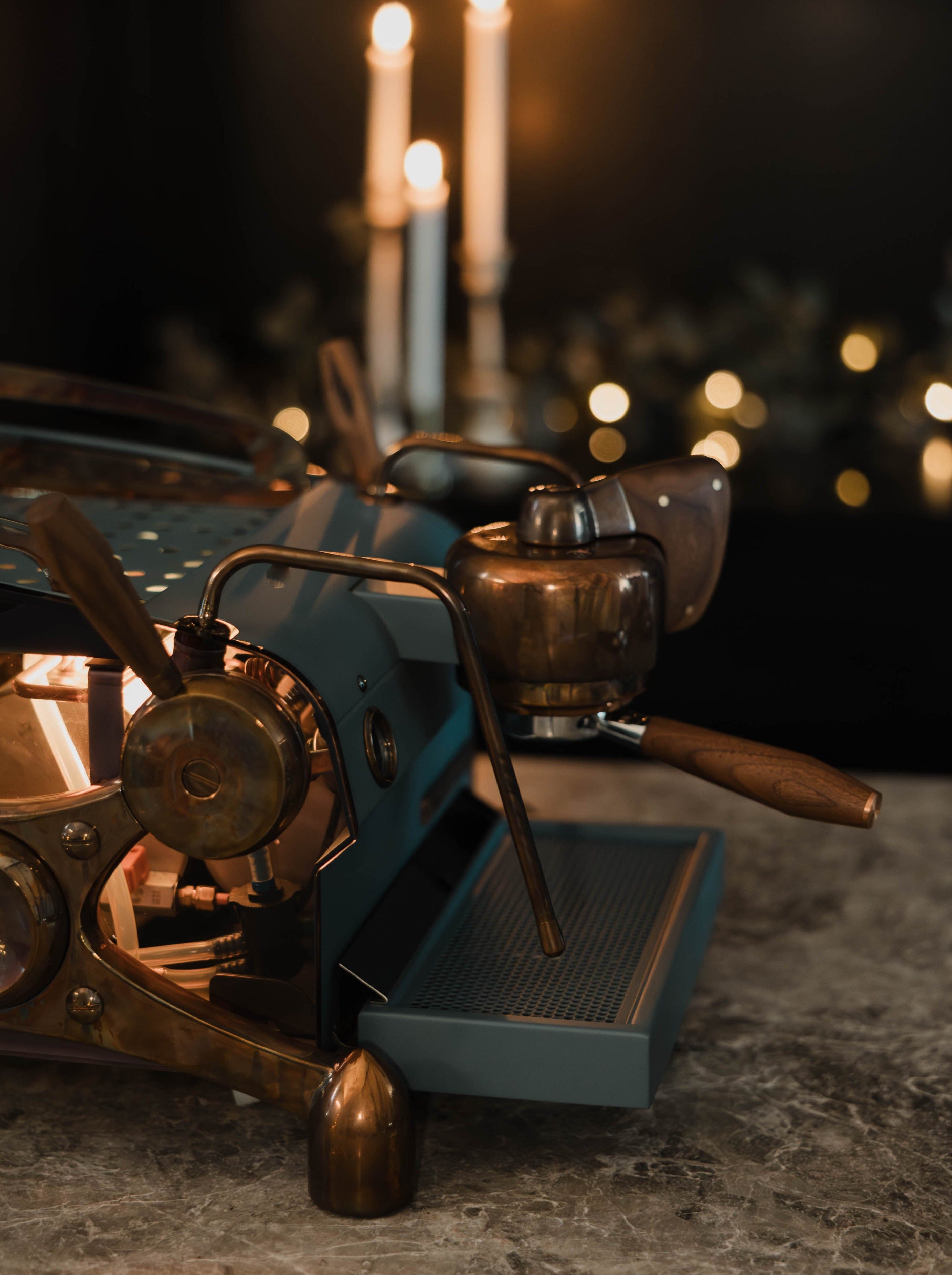 The side of a deep blue, bespoke Slayer Single Group espresso machine with burnt copper highlights and walnut accents, showing its lit interior through smoky side panels.