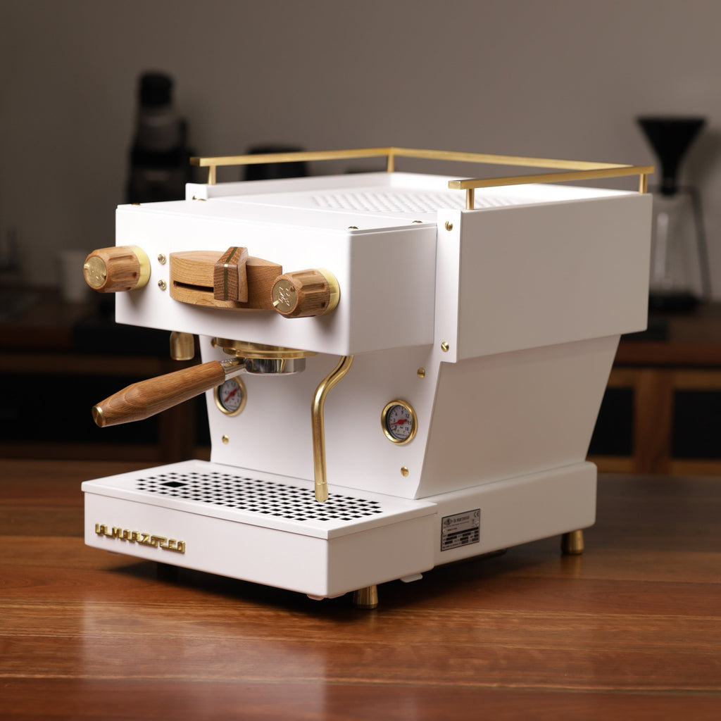 A white, Specht La Marzocco Linea Mini espresso machine with polished brass and oak wood accents.